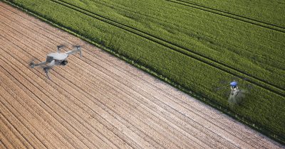 Drone multirotor DJI Air2S realizando o mapeamento aéreo de uma lavoura enquanto um drone agrícola pulverizador aplica insumos na plantação
